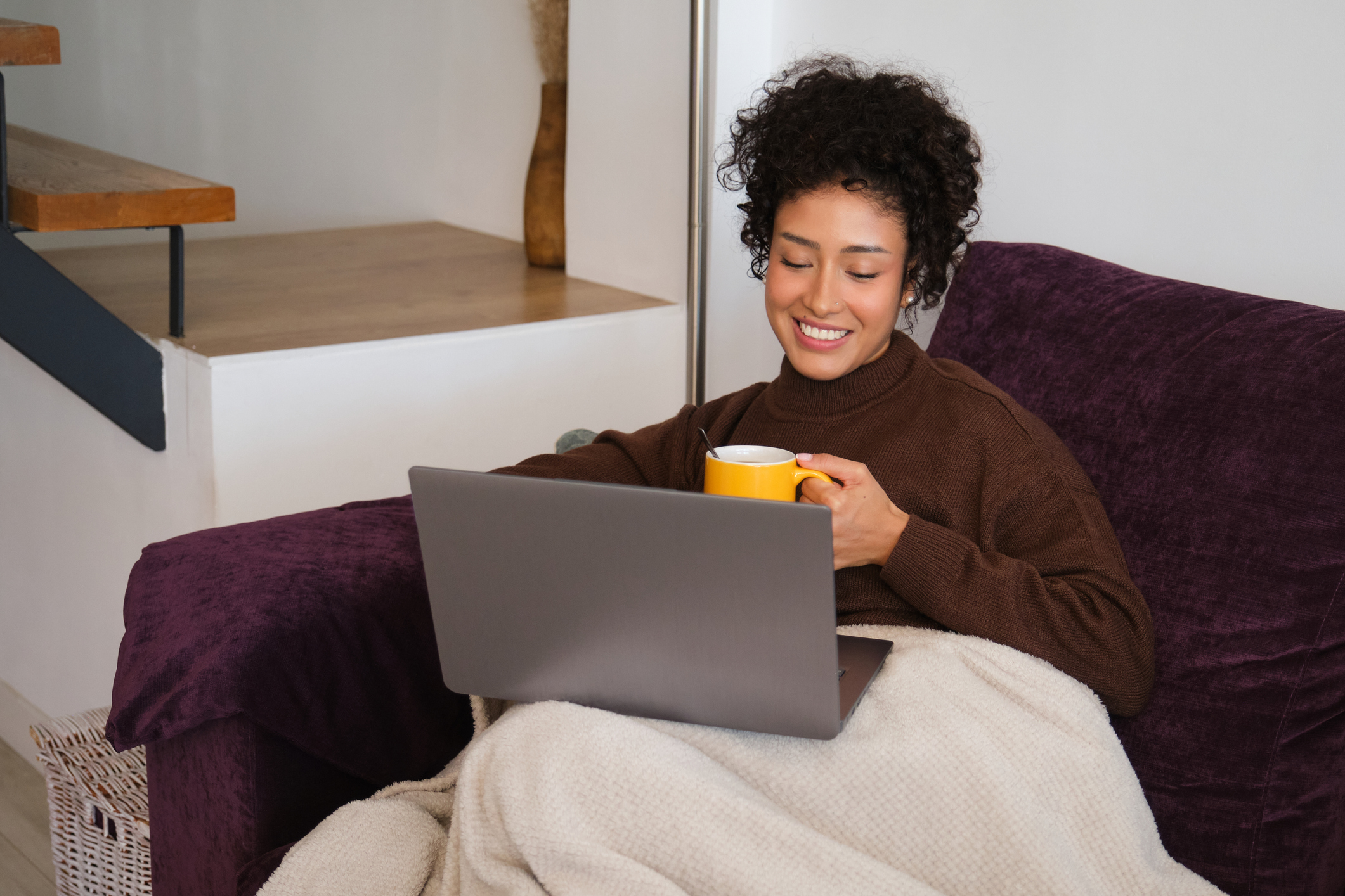 Young woman relaxing on sofa, working on laptop and drinking tea